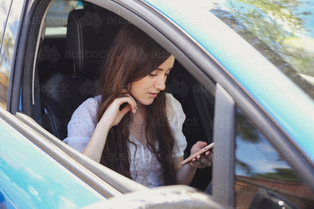 Teenage girl using mobile phone, waiting in the car - Australian Stock Image