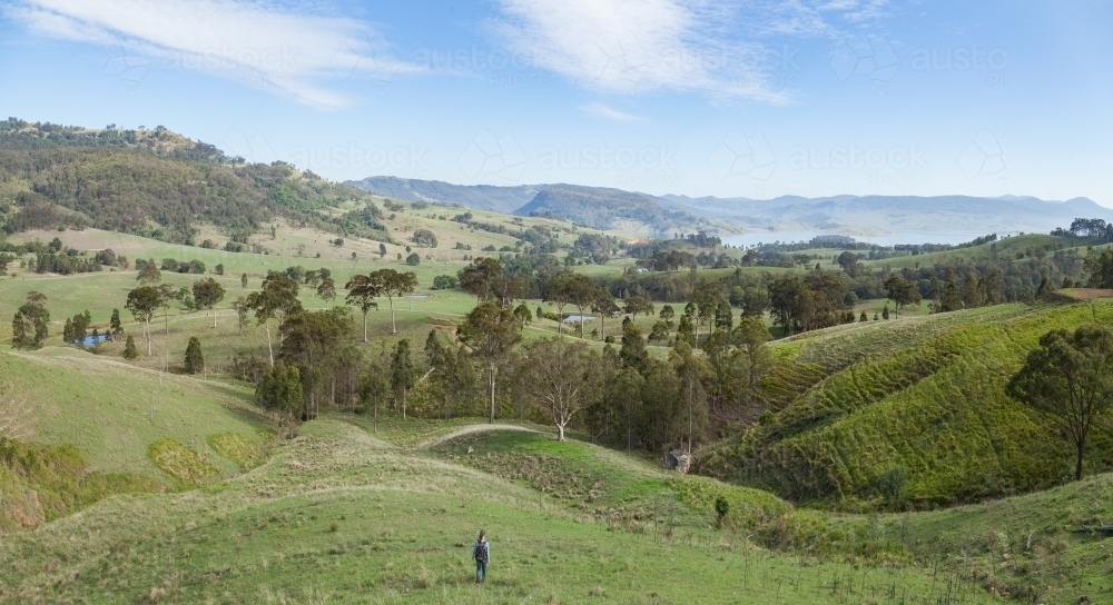 Teenage girl walking down grassy slope to green valley - Australian Stock Image