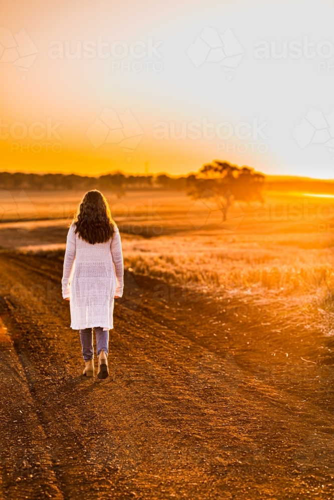 Teenage girl walking on dirt road at sunset - Australian Stock Image
