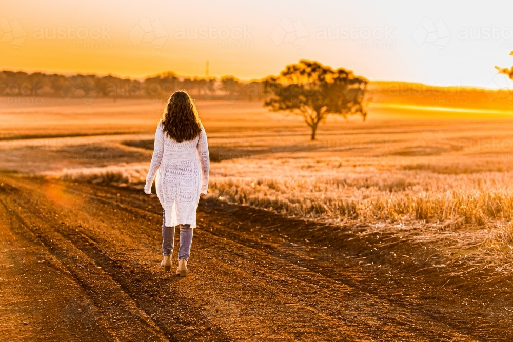 Teenage girl walking on dirt road at sunset - Australian Stock Image
