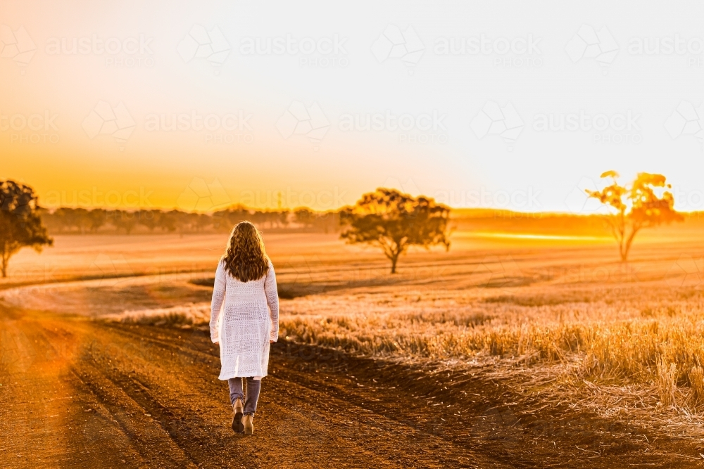 Teenage girl walking on dirt road at sunset - Australian Stock Image