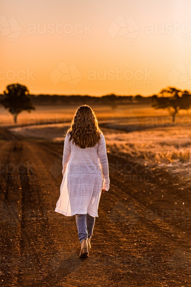 Teenage girl walking on dirt road at sunset - Australian Stock Image