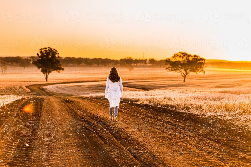 Teenage girl walking on dirt road at sunset - Australian Stock Image