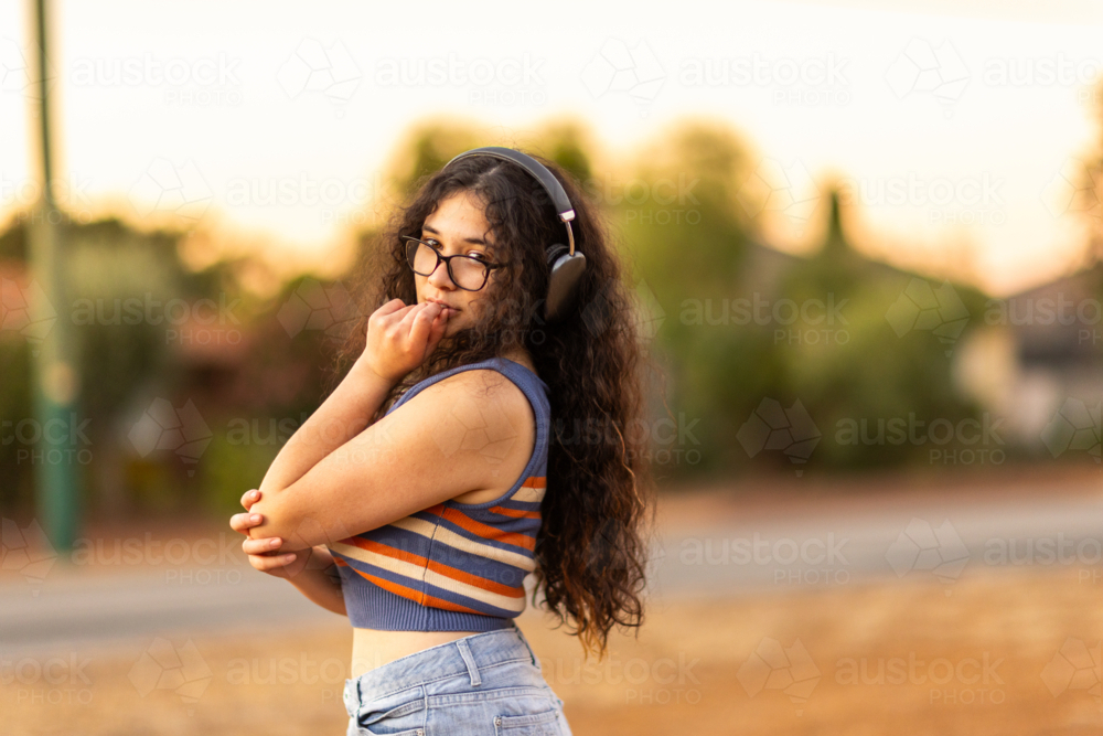 Teenage girl with dark curly hair wearing headphones outdoors - Australian Stock Image