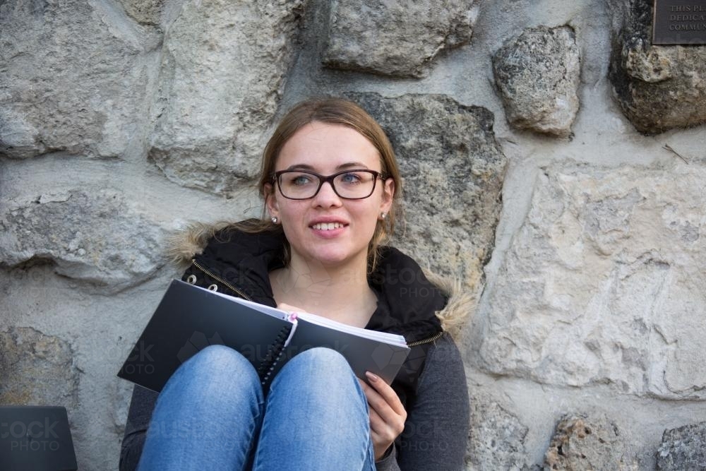 Teenage girl with glasses writing in notebook - Australian Stock Image