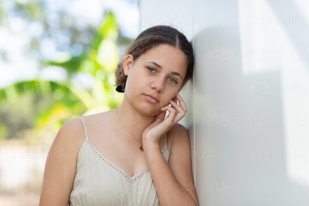 Teenage girl with hand to face leaning against white wall - Australian Stock Image