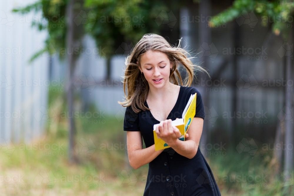 Teenage girl with long hair reading a book outside - Australian Stock Image