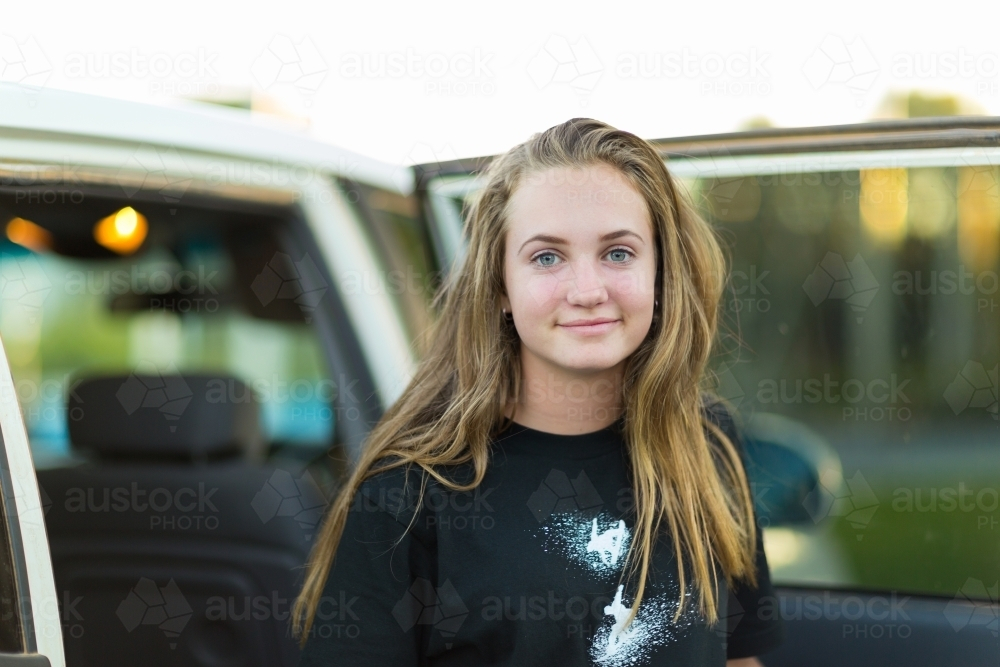 Teenage girl with long hair standing beside the car with open door - Australian Stock Image