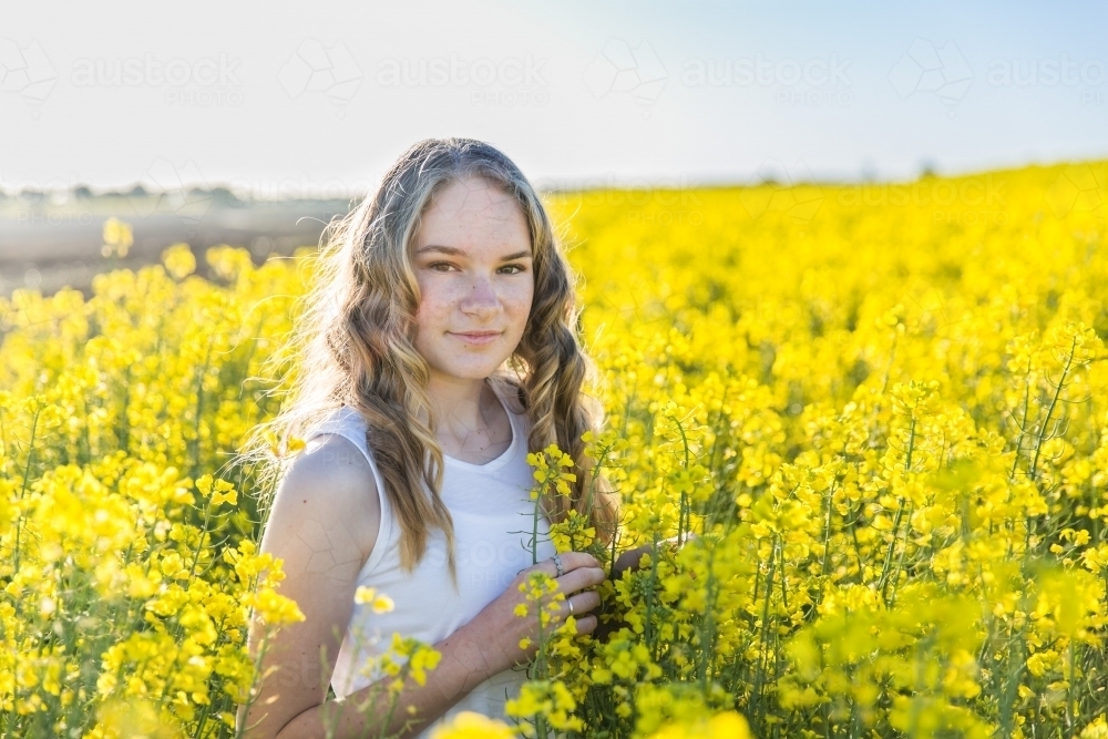 Teenage girl with small smile standing on farm in field of canola - Australian Stock Image