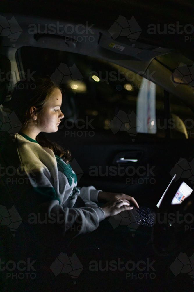 Teenage girl working on laptop in car at night - Australian Stock Image