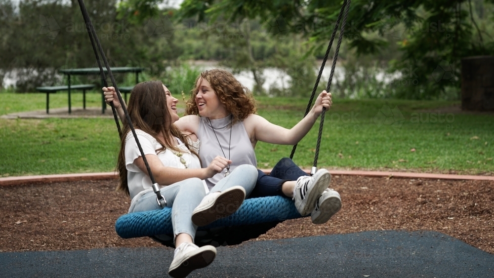 Teenage girlfriends on park swing - Australian Stock Image