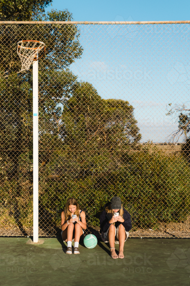 Teenage girls on phones at outdoor netball court - Australian Stock Image