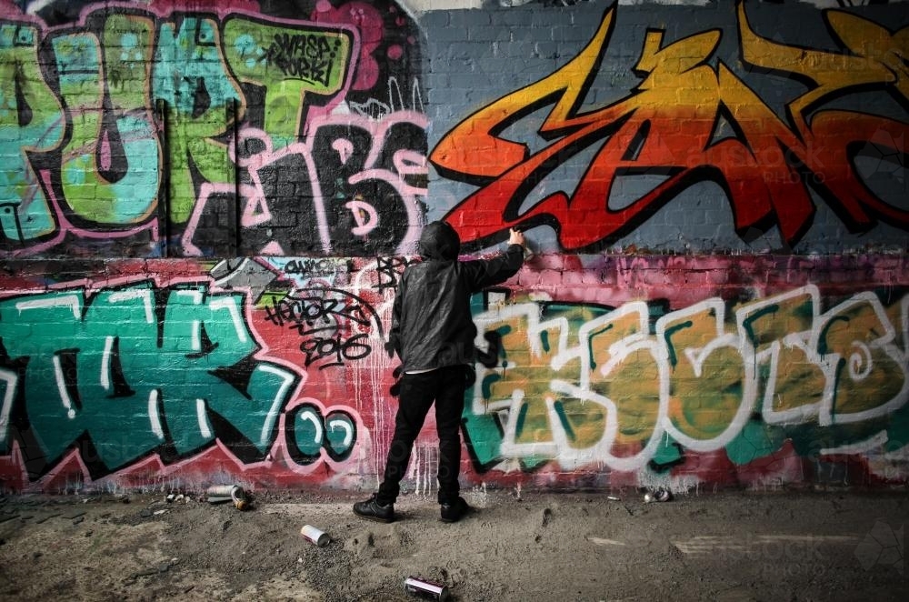 Image of Teenage graffiti artist spray painting a wall - Austockphoto