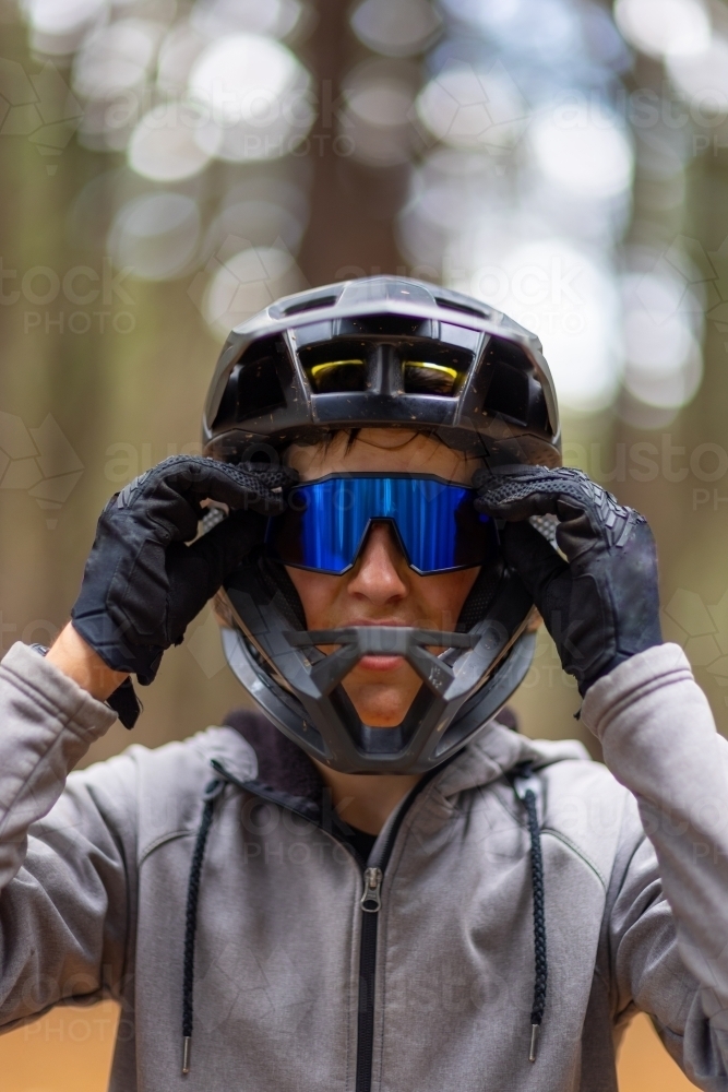 Image of teenage mountain bike rider with full face helmet and gloves, adjusting sunglasses