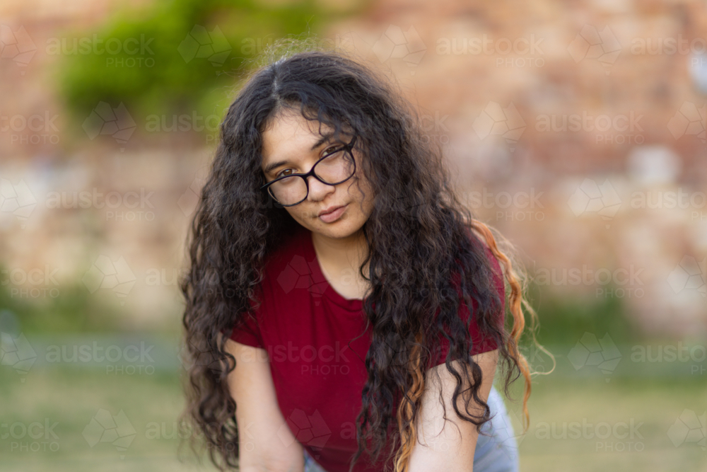 teenaged girl with glasses leaning forward with long dark curly hair falling over her shoulders - Australian Stock Image
