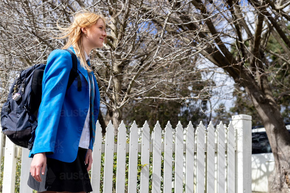 Image of Teenaged schoolgirl in uniform walking past white picket fence ...