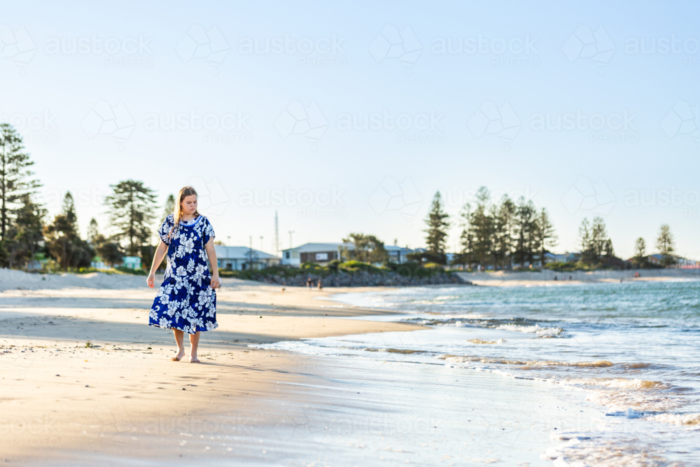 Teenaged Torres Strait Islander girl walking along coastal shoreline in traditional floral dress - Australian Stock Image