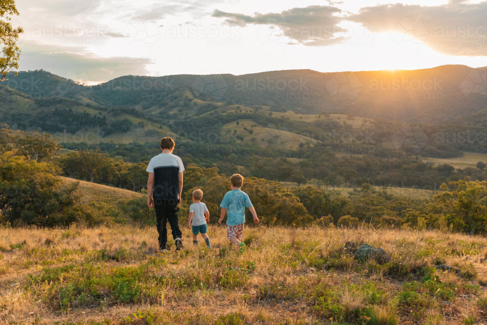 Teenager and two little boys exploring hilltop in regional New South Wales at sunset - Australian Stock Image