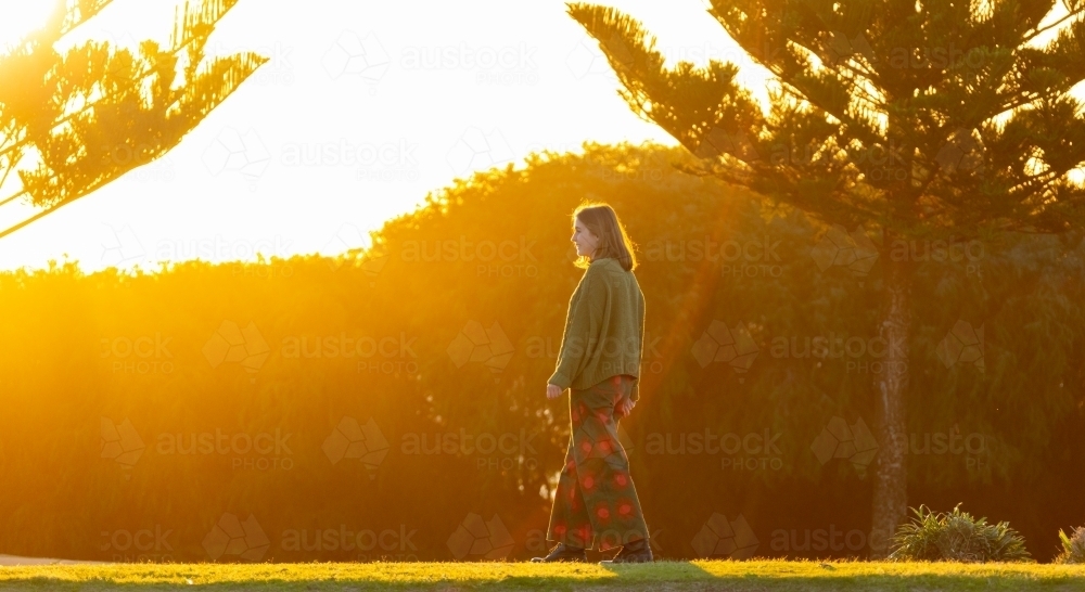 teenager back-lit walking past pine trees in coastal park - Australian Stock Image