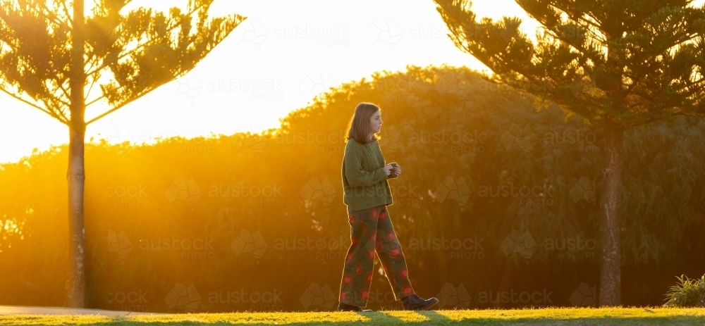 teenager back-lit walking past pine trees in coastal park - Australian Stock Image