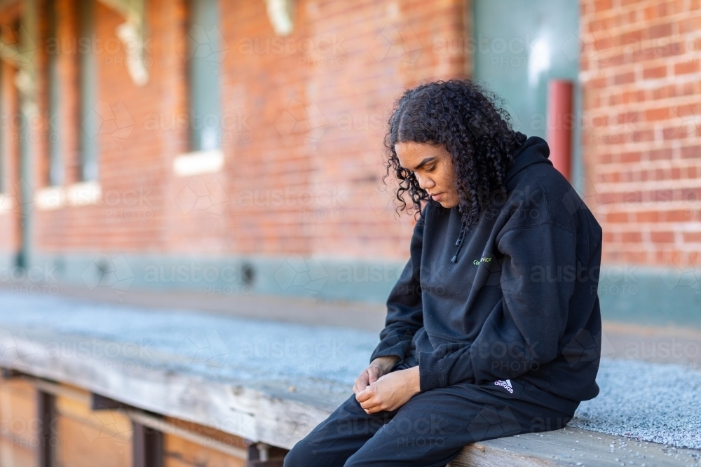 teenager dressed in black looking down sitting on platform - Australian Stock Image