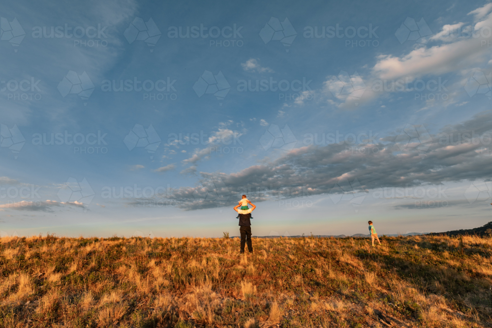 Teenager giving happy little boy a shoulder ride with a blue sky background - Australian Stock Image