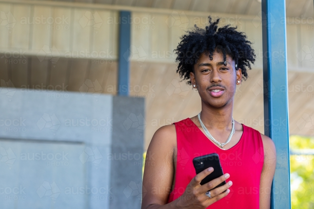 teenager holding smartphone while leaning on a post - Australian Stock Image