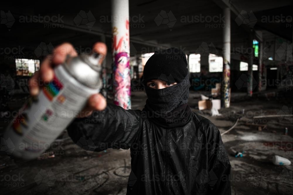 Teenager holding spray paint can in disused warehouse - Australian Stock Image