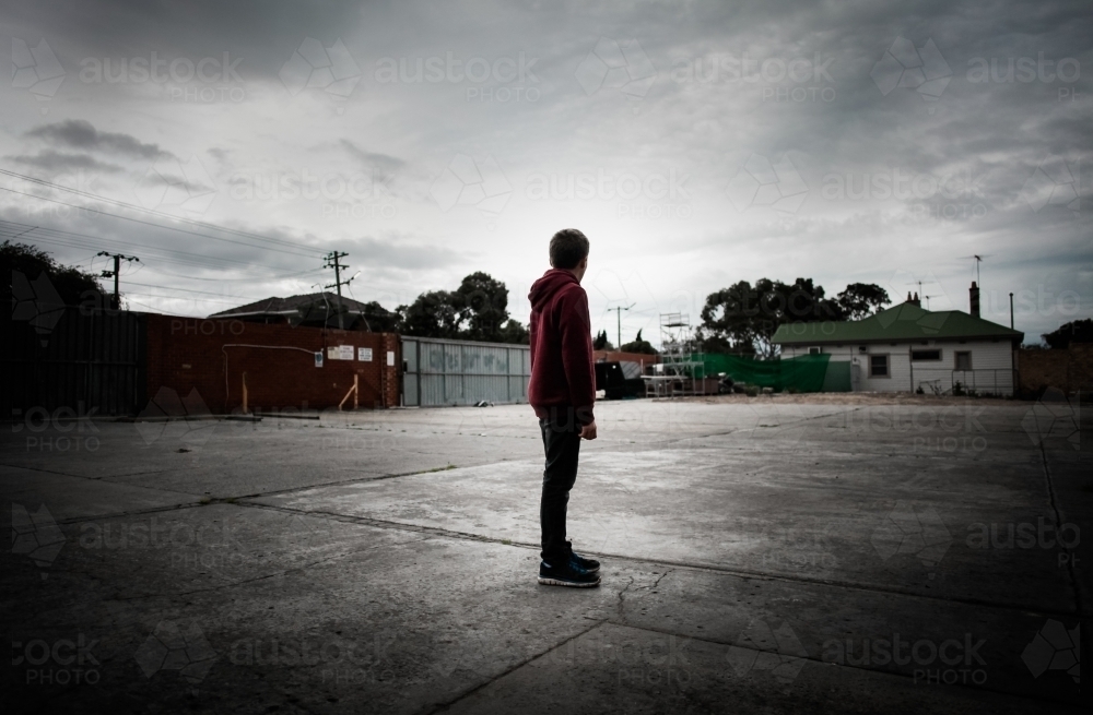 Teenager in a deserted parking lot looking into the distance - Australian Stock Image