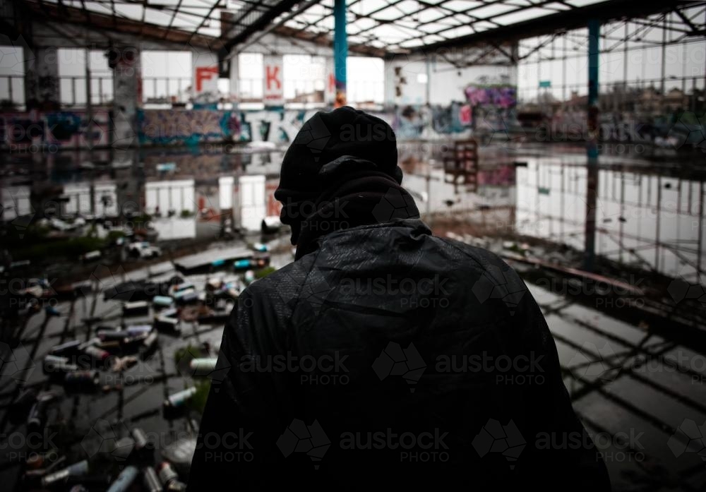 Teenager in disused warehouse surrounded in empty spray cans - Australian Stock Image