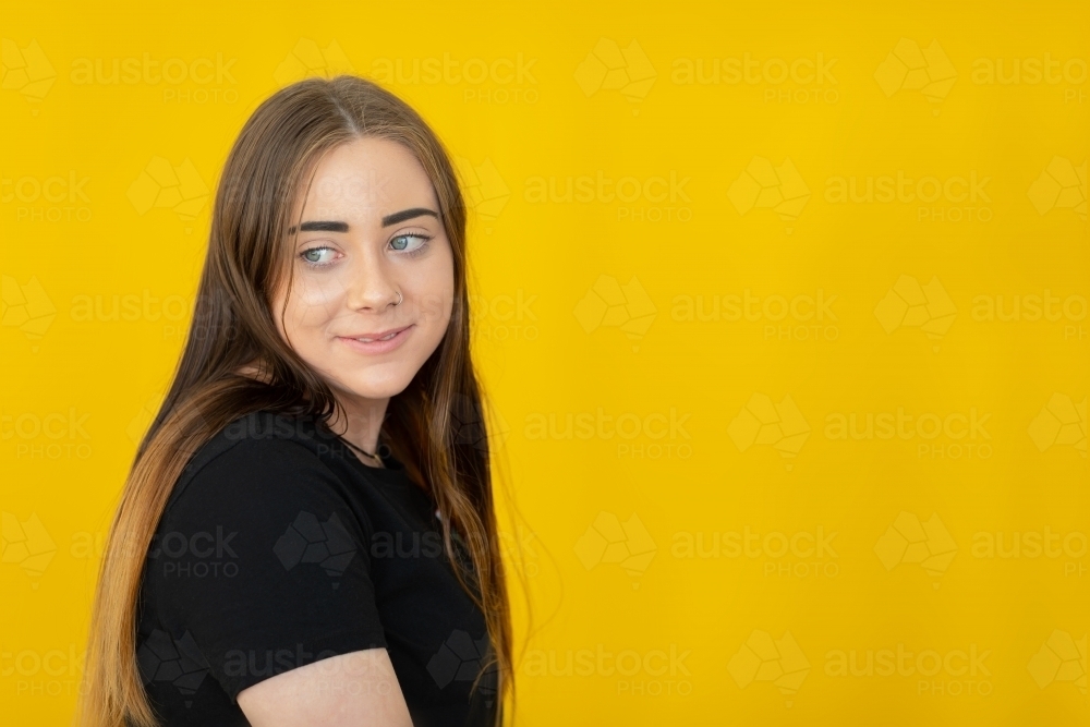 teenager looking sideways over shoulder on yellow background - Australian Stock Image