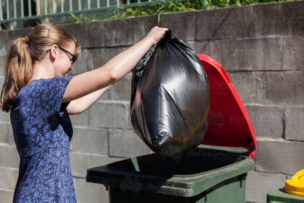 Teenager putting bag of rubbish in red bin - Australian Stock Image