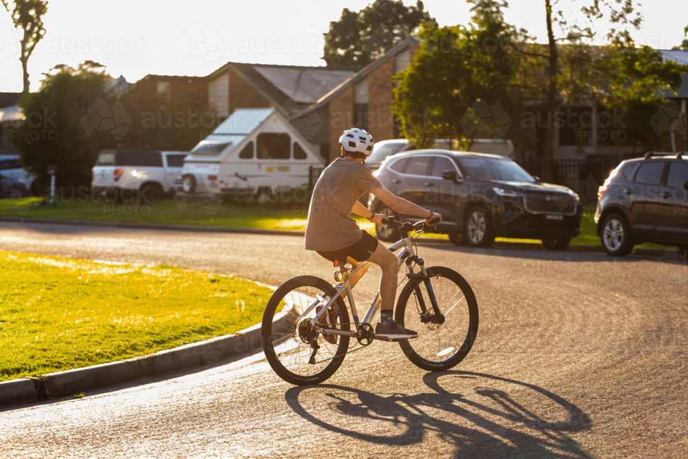 Teenager riding bike wearing helmet for safety on street in town - Australian Stock Image