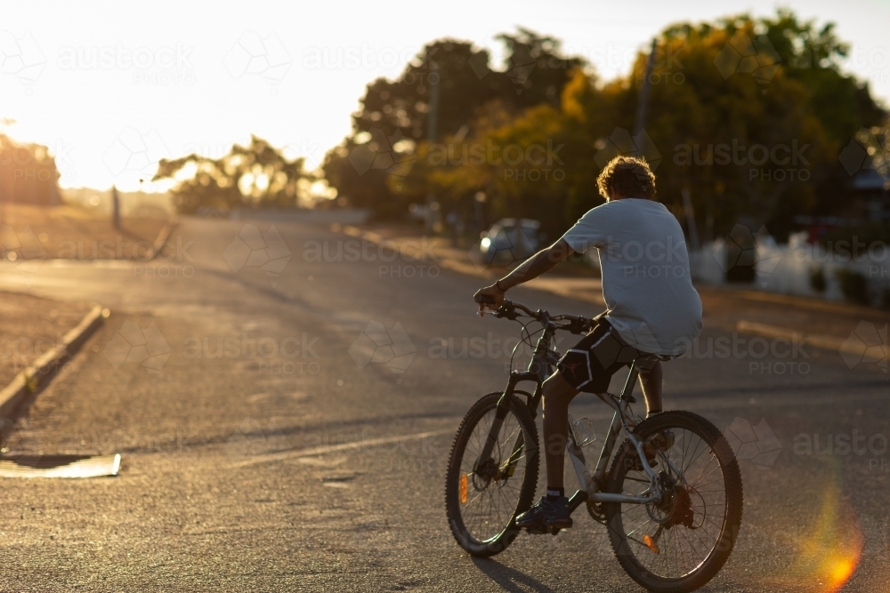 teenager riding bike with no helmet on quiet evening street - Australian Stock Image