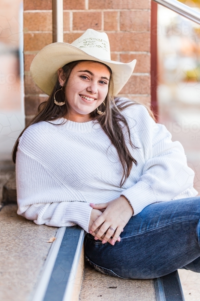 Teenager sitting leaning on step wearing hat and smiling - Australian Stock Image