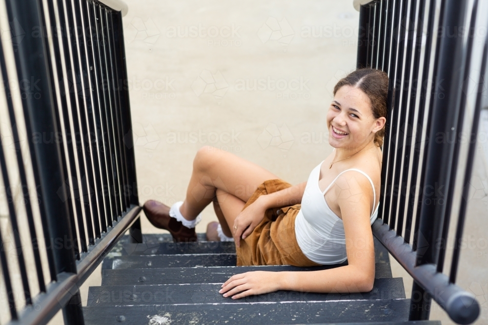 Teenager sitting on stairs looking up smiling - Australian Stock Image