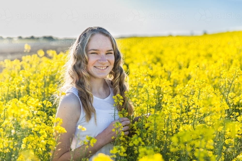 Teenager standing on farm in canola crop smiling - Australian Stock Image