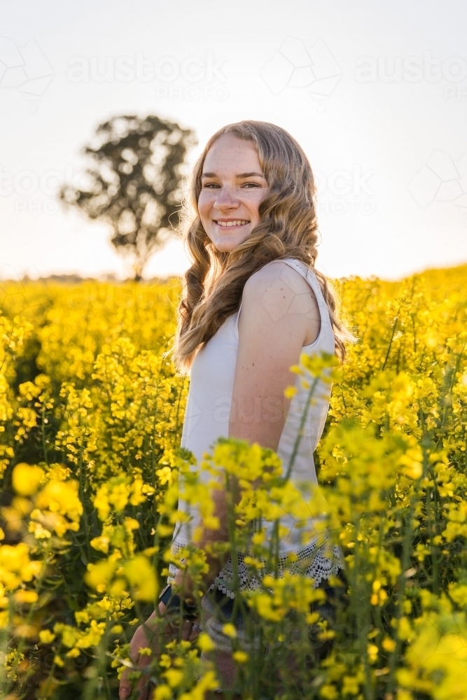 Teenager standing on farm in canola field smiling - Australian Stock Image