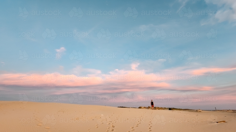 Teenager standing on the sand dunes at Birubi Beach at sunset - Australian Stock Image