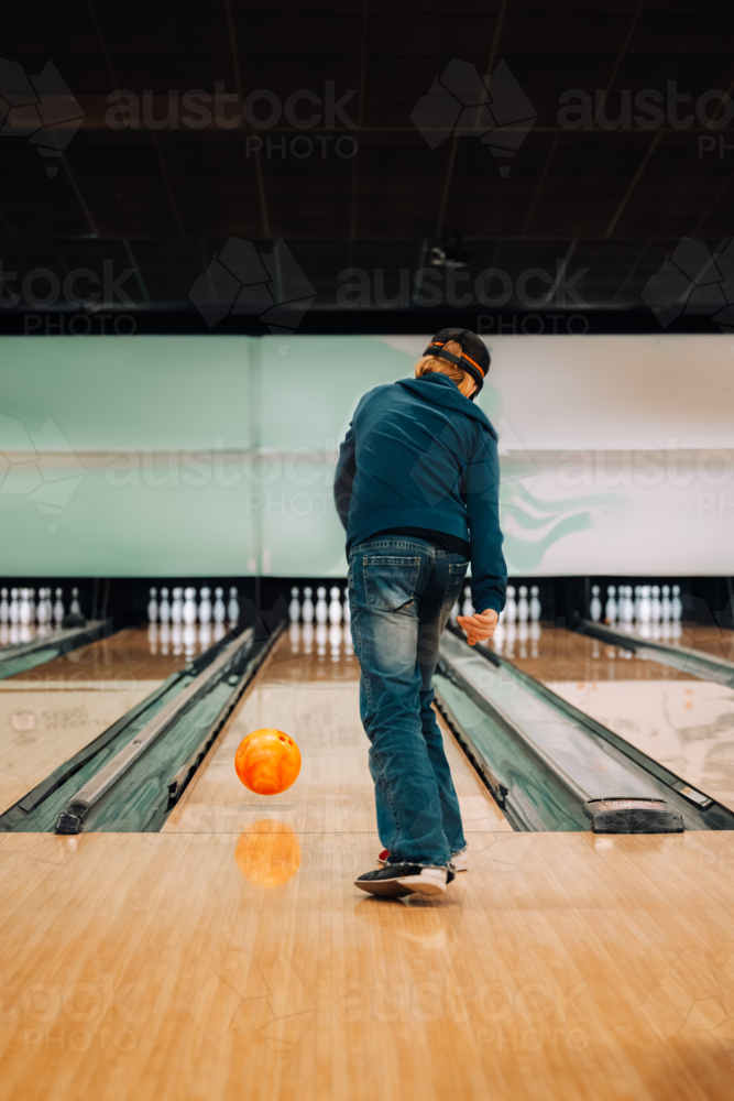 Teenager ten pin bowling in brightly lit bowling alley - Australian Stock Image