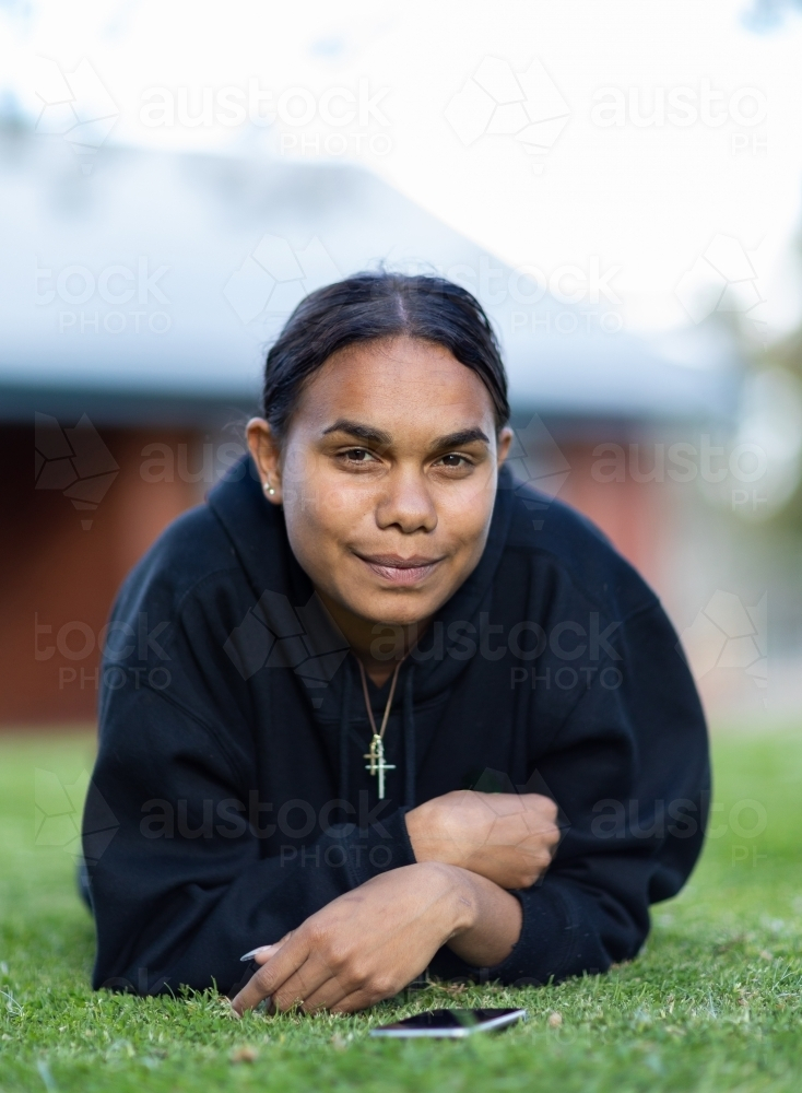 teenager wearing dark hoodie laying down on lawn - Australian Stock Image