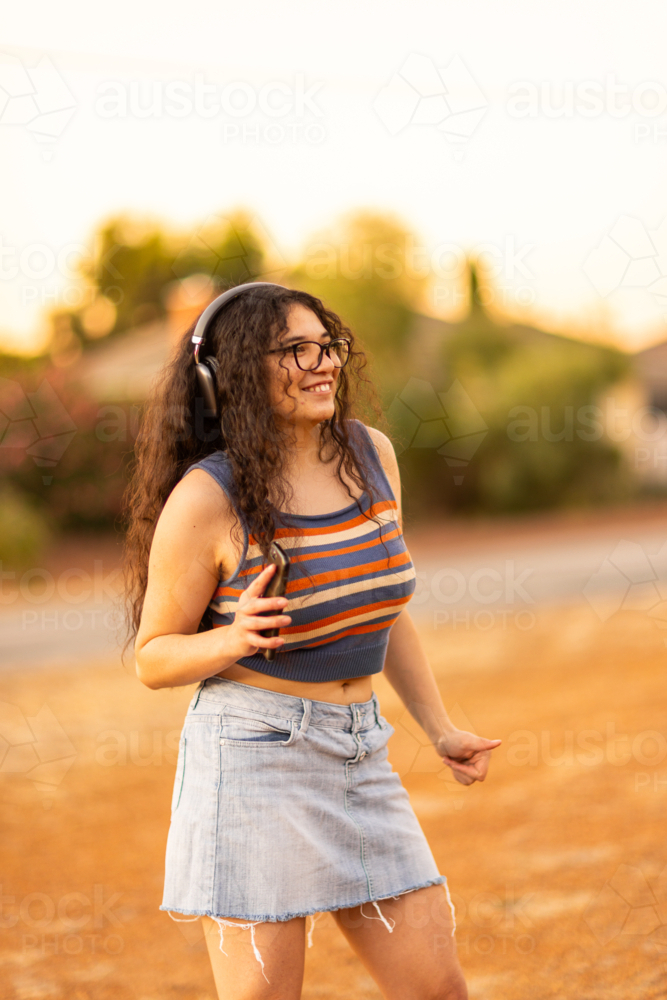 teenager with headphones dancing to music outside at sunset - Australian Stock Image