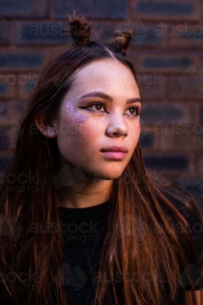 teenager with space buns and glitter makeup against a dark background - Australian Stock Image