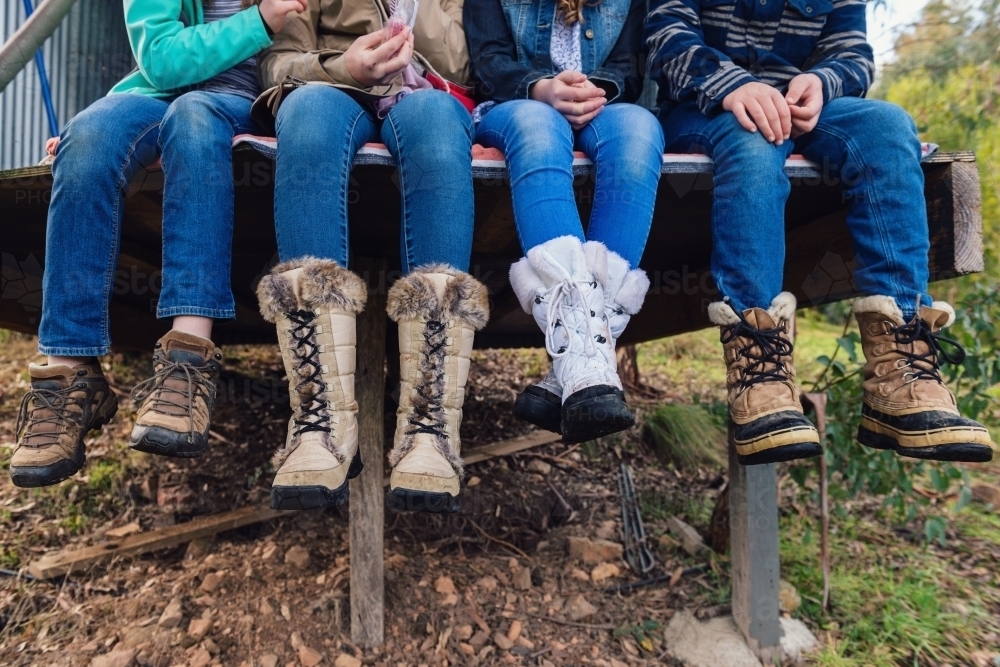 teenagers sitting outdoors, all wearing jeans and warm boots - Australian Stock Image