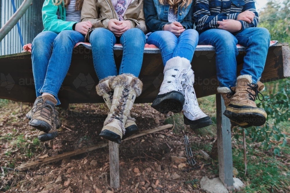 teenagers sitting outdoors, all wearing jeans and warm boots - Australian Stock Image