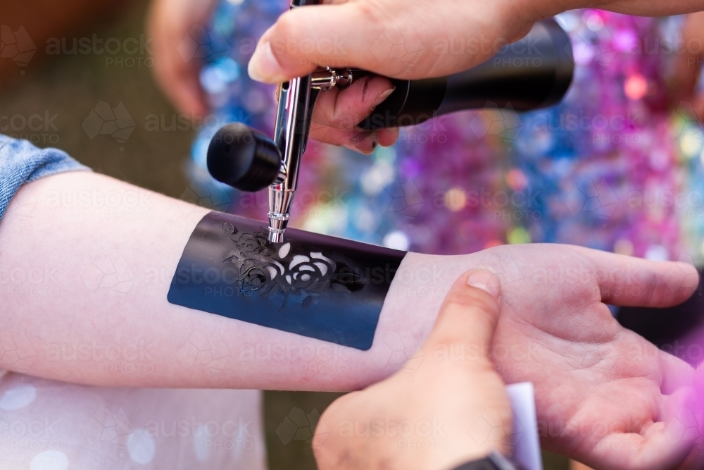 Temporary Airbrush Tattoo being sprayed on persons arm at event with spray gun - Australian Stock Image