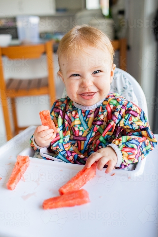 Image of Ten month old baby eating watermelon on summer day in high