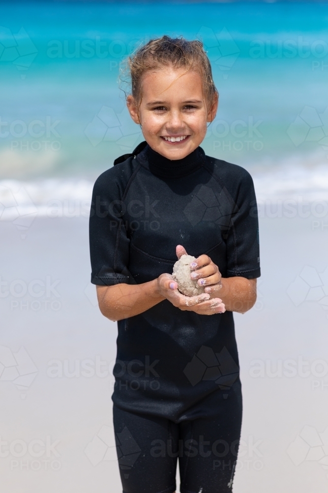 Image of ten year old girl in wetsuit on the beach making a sand ball