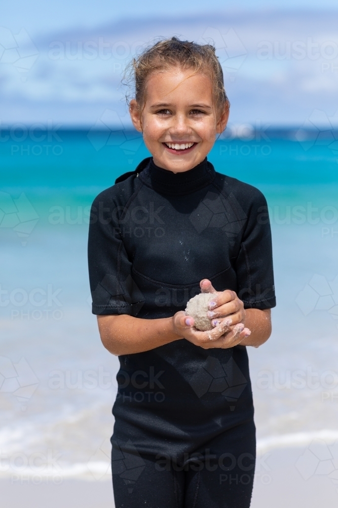 ten year old  girl in wetsuit on the beach making a sand ball - Australian Stock Image