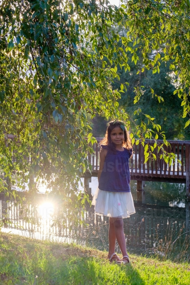 Ten year old girl standing on grass beside dam in park - Australian Stock Image